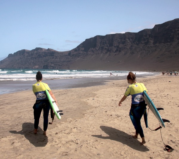 2 chicas van hacia las olas en la playa de Famara en Lanzarote